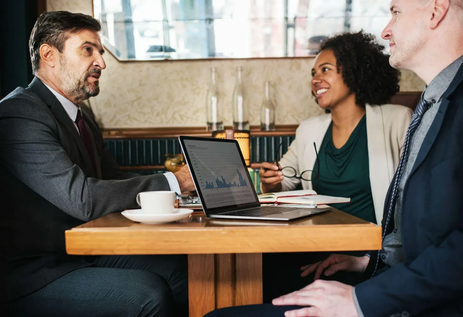 Three business colleagues reviewing a laptop together across a café table.
