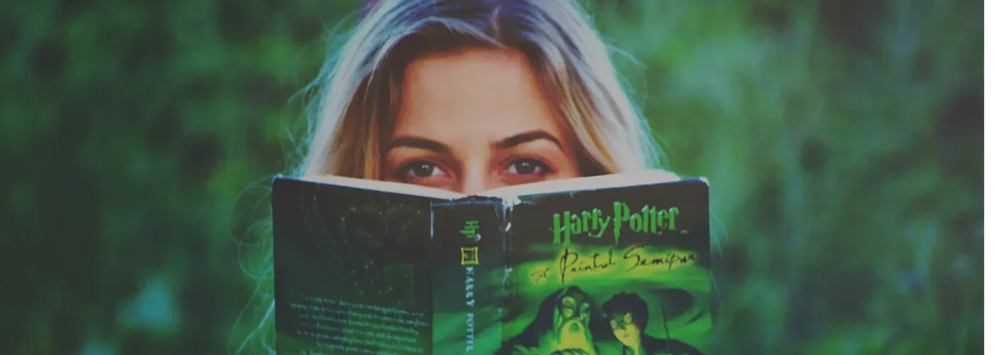A person reading a Harry Potter book, framed by green foliage.